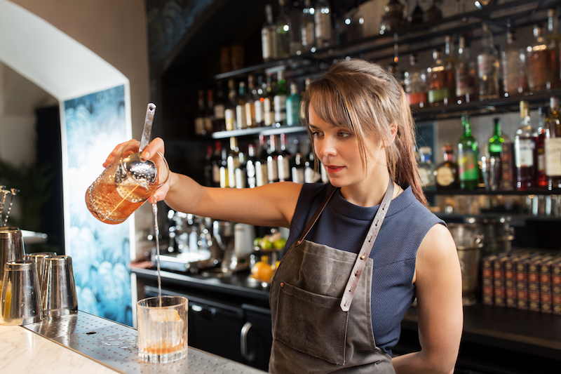 barmaid with glass and jug preparing cocktail