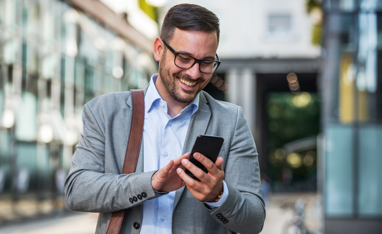 Young smiling businessman on the way to the office searching information on the internet with smartphone. Business, education, lifestyle concept